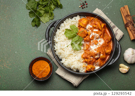 Indian dish chicken tikka masala served with rice and spices on green background top view, copy space Indian dish chicken tikka masala served with rice and spices on green background top view, copy space 129293542
