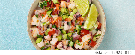 Peruvian seafood ceviche with shrimps, octopus, tomatoes, cucumber, and parsley in a bowl served with lime top view 129293810