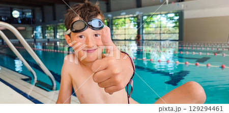 Happy boy giving a thumbs up in an indoor swimming pool. Concept of self-confidence in children's swimming lessons, child development, children's sports Happy boy giving a thumbs up in an indoor swimming pool. Concept of self-confidence in children's swimming lessons, child development, children's sports 129294461