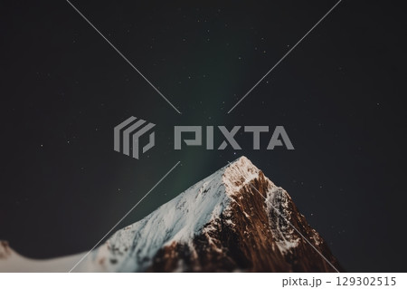 Snowy mountain peak under a starry night sky with northern lights visible 129302515