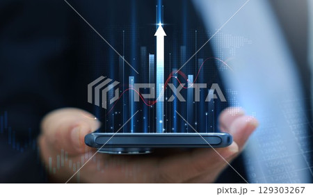 Businessman holding smartphone with glowing stock market chart and upward arrow. Financial growth, investment success, fintech, and trading technology concept. business stock market. 129303267