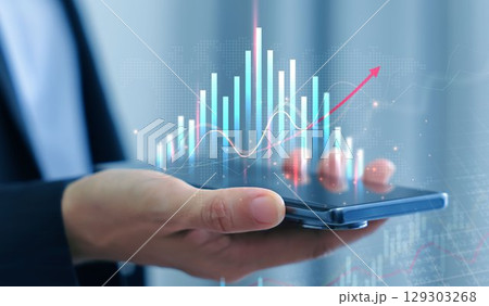 Businessman holding smartphone with glowing stock market chart and upward arrow. Financial growth, investment success, fintech, and trading technology concept. business stock market. 129303268