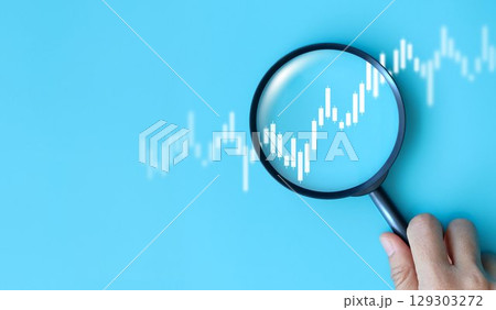 Hand holding magnifying glass analyzing digital financial stock chart. Data analysis, investment research, trading strategy, and financial market concept on blue background. business stock market. Hand holding magnifying glass analyzing digital financial stock chart. Data analysis, investment research, trading strategy, and financial market concept on blue background. business stock market. 129303272