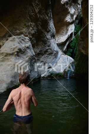 Man Exploring a Scenic Natural Canyon Pool with a Waterfall 129304252