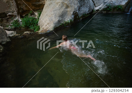 A Woman Swims in a Tranquil Rock-Surrounded Stream A Woman Swims in a Tranquil Rock-Surrounded Stream 129304254