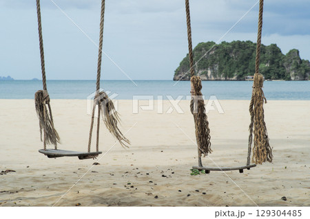 Couple of wooden swings on the beach with blurred seascape and island in background 129304485