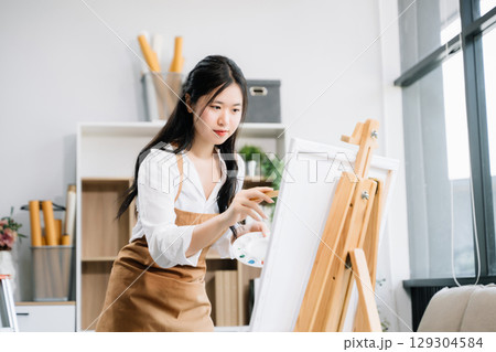 Asian Female painter do artwork in art workshop, painting supplies, oil pastels, two canvas easel, creative space with paintbrush in art studio Asian Female painter do artwork in art workshop, painting supplies, oil pastels, two canvas easel, creative space with paintbrush in art studio 129304584