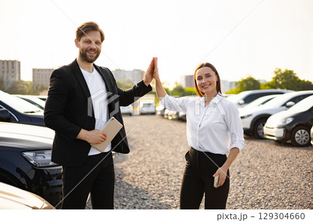 A male car dealer and a female customer celebrate a car purchase with a high-five gesture at the dealership. A male car dealer and a female customer celebrate a car purchase with a high-five gesture at the dealership. 129304660