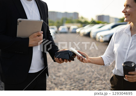 A car dealer assisting a female customer with a purchase, using a mobile payment system at a car dealership. 129304695