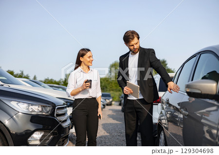 A male car dealer showing a car to a woman customer at a dealership. A male car dealer showing a car to a woman customer at a dealership. 129304698