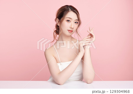 A beautiful young Asian woman with clean, fresh skin against a pink background. Skincare, facial treatment, cosmetology, beauty, and spa. An elegant portrait of an Asian woman. A beautiful young Asian woman with clean, fresh skin against a pink background. Skincare, facial treatment, cosmetology, beauty, and spa. An elegant portrait of an Asian woman. 129304968