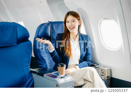 Asian female passenger of airplane sitting in comfortable seat while working laptop and tablet. Travel in style, Asian female passenger of airplane sitting in comfortable seat while working laptop and tablet. Travel in style, 129305337