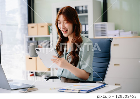 Beautiful Asian business woman typing laptop and tablet Placed at the table 129305455