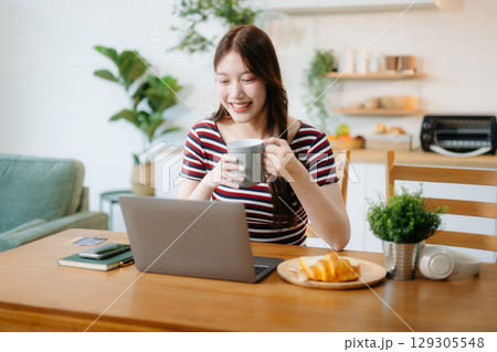 oung Asian woman with sitting working on laptops and tablets in a cozy workspace. Perfect for education, innovation, 129305548