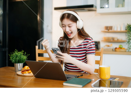 Happy woman with headphones working on a tablet in a bright kitchen. Ideal for themes of remote work 129305590