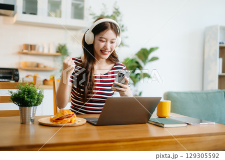 oung Asian woman with sitting working on laptops and tablets in a cozy workspace. Perfect for education, innovation, 129305592