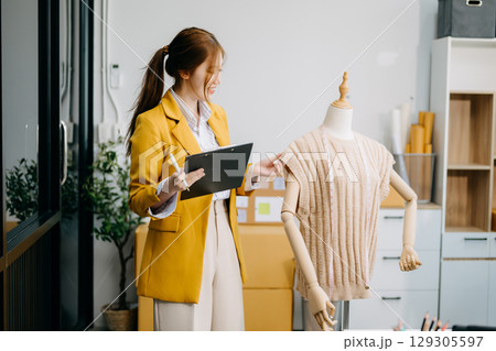Asian tailor woman working on clothes in tailoring atelier. beautiful young female fashion designer smile Asian tailor woman working on clothes in tailoring atelier. beautiful young female fashion designer smile 129305597