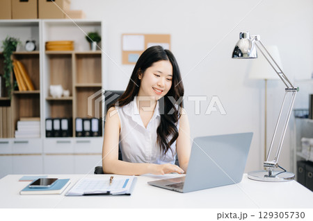 Asian Businesswoman Analyzing Finance on Tablet and Laptop at modern Office Desk tax, report, accounting, statistics 129305730