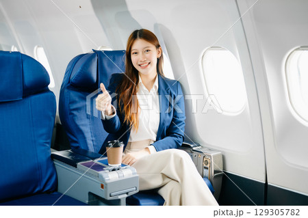 Asian female passenger of airplane sitting in comfortable seat while working laptop and tablet. Travel in style, 129305782