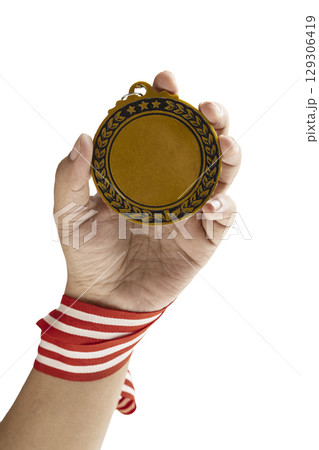 Human hand holding golden award medal suspended from a red and white striped ribbon isolated over a white background. Copy space. Symbol of achievement, recognition, or competition 129306419