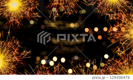 Sparkling border of glowing sparklers against a bokeh blurred backdrop of lights at night. Copy space Sparkling border of glowing sparklers against a bokeh blurred backdrop of lights at night. Copy space 129306478