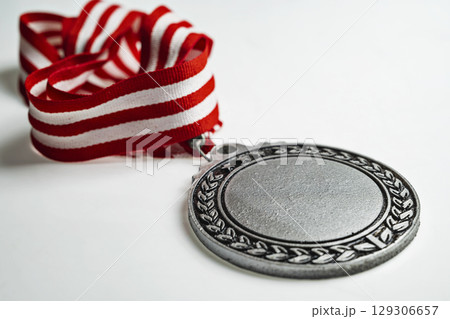 Closeup view of the silver award medal suspended from a red and white striped ribbon isolated over a white background. Copy space. Symbol of achievement, recognition, or competition 129306657