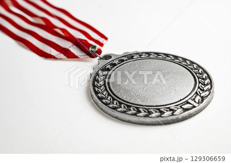 Closeup view of the silver award medal suspended from a red and white striped ribbon isolated over a white background. Copy space. Symbol of achievement, recognition, or competition 129306659