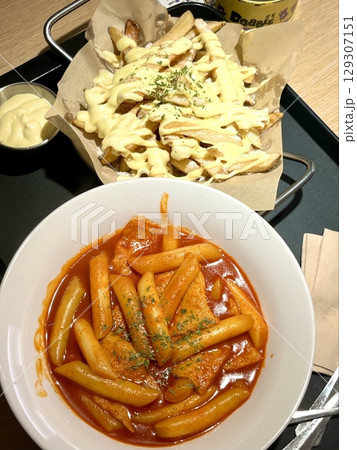 Spicy and chewy tteokbokki paired with crispy potato wedges, creating a perfect balance of heat and crunch for a satisfying Korean street food experience. 129307151