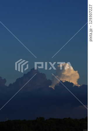 気象　積雲　雄大雲。八月の夕方、日が落ちた場所の黒い雲と未だに日差しを浴びて発達中の白い雲 129307227