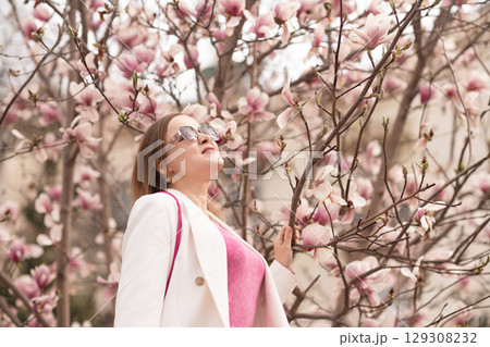 Magnolia Bloom Woman: Springtime lady looks up at pink flowers in park enjoying beauty. 129308232