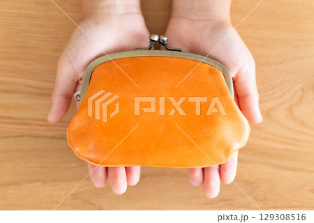 オレンジのがま口財布を持つ小学生の男の子の手 129308516