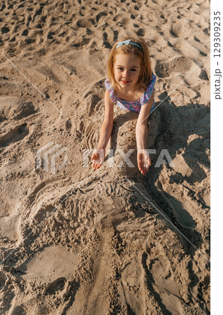 Child playing in sand creating a sand sculpture on a sunny beach during the afternoon Child playing in sand creating a sand sculpture on a sunny beach during the afternoon 129309235