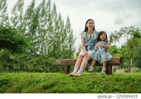 happy mother and toddler girl sitting on a wooden bench and talking together in park 129309433