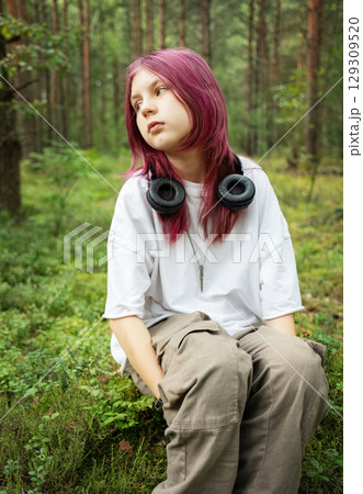 Youngster with pink hair enjoying nature's sounds in lush forest Youngster with pink hair enjoying nature's sounds in lush forest 129309520