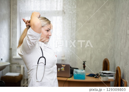 A professional healthcare worker in a medical coat fixes her hair, her stethoscope around her neck, ready for the day's demands. A professional healthcare worker in a medical coat fixes her hair, her stethoscope around her neck, ready for the day's demands. 129309803