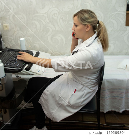 Doctor on phone using medical machine, white coat, diagnostic equipment. Medical call center employee in the doctor's office working. 129309804