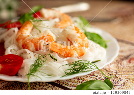 rice noodles with shrimp and tomato slices on a wooden table 129309845