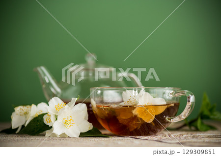 Aromatic tea with jasmine flowers in a glass cup on a green background Aromatic tea with jasmine flowers in a glass cup on a green background 129309851