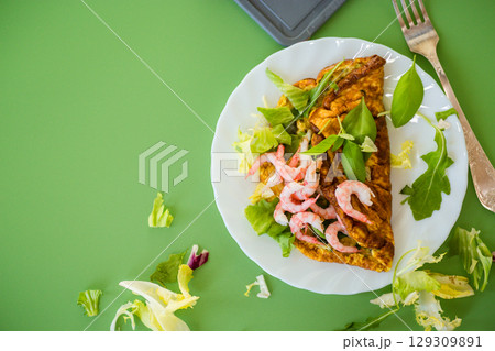 Omelette with seafood and greens in a white plate on a green background Omelette with seafood and greens in a white plate on a green background 129309891