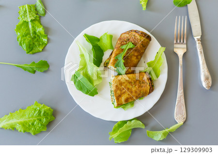 Appetizing omelette with greens and arugula on a white plate 129309903