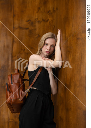 A fashion model is captured from a back-facing perspective, holding a rich brown leather backpack and looking away, showcasing the product in a minimalist setting. A fashion model is captured from a back-facing perspective, holding a rich brown leather backpack and looking away, showcasing the product in a minimalist setting. 129309991