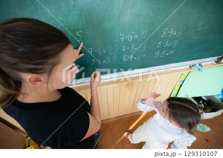 Math lesson with teacher and student at chalkboard, focusing on multiplication and calculations in classroom environment. 129310107