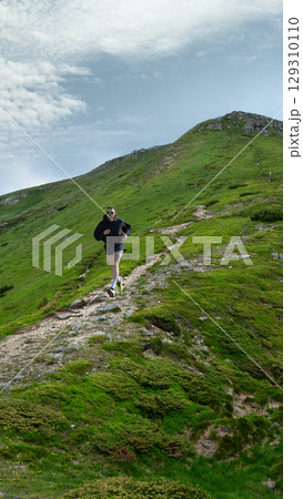 Bold poster of man in black running uphill on winding rocky mountain path in green landscape Bold poster of man in black running uphill on winding rocky mountain path in green landscape 129310110
