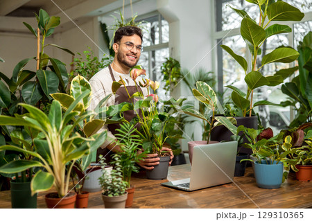Young man sitting at the laptop in the flower shop Young man sitting at the laptop in the flower shop 129310365
