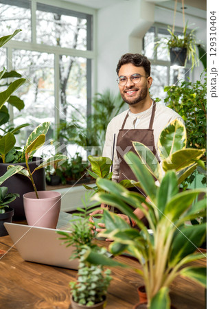 Young man in eyeglasses in the flower shop looking contented and smiling 129310404