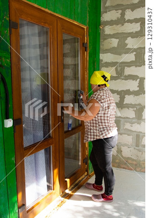 Cleaning the window glass of the wooden framed windows. Woman wearing headscarf, using cloth and cleaner for spotless shine. Door, green walls. 129310437