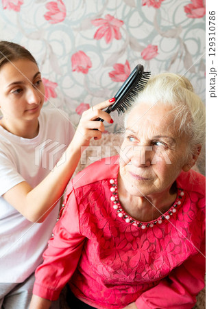 Care and connection shine in a moment shared between a young girl and her grandmother in a cozy living room filled with warmth and love during a sunny afternoon 129310786