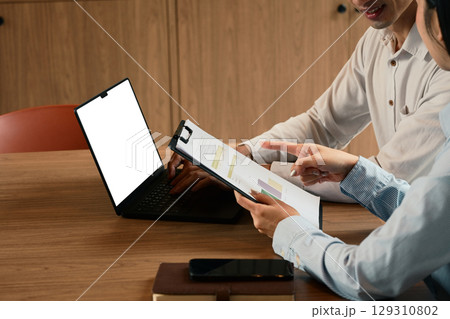 Two coworkers using laptop, working on financial reports and charts at modern office 129310802