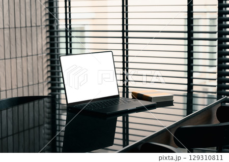 Modern workspace with laptop and book on sleek black table near window blinds in a stylish office 129310811