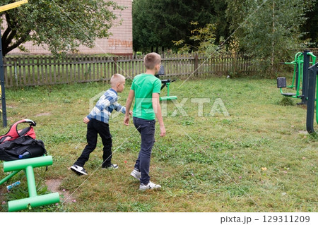 Two young boys are playing in a yard with exercise equipment, enjoying a playful moment in a grassy outdoor space. 129311209